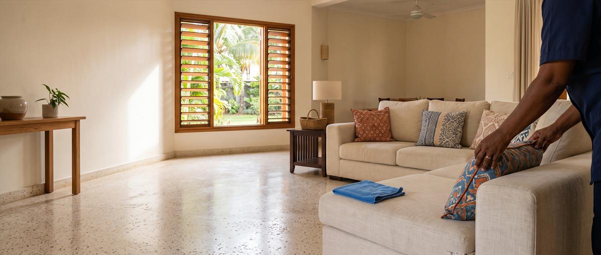 A Home Care Professional plumping cushions on a sofa in a bright Mauritian living room
